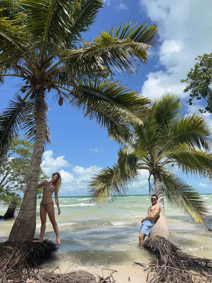 Carola and Martín leaning on palm trees on a tropical beach